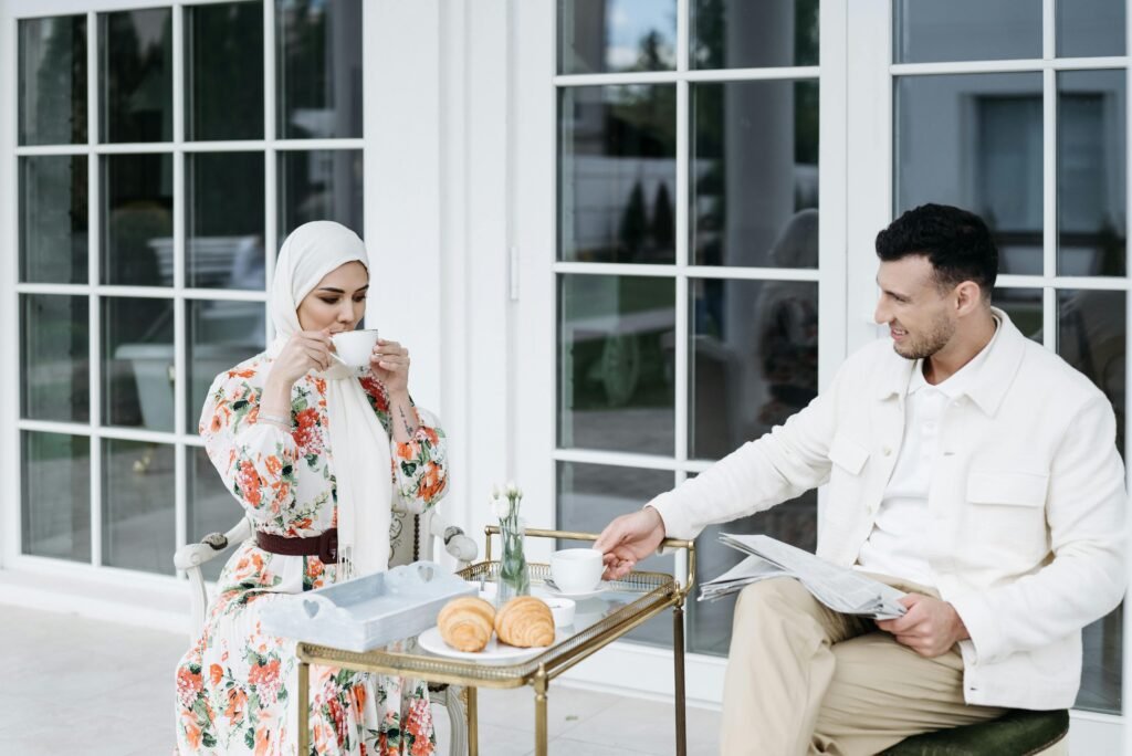 A Muslim couple enjoying a serene breakfast outdoors, sharing coffee and pastries on a sunny day.
